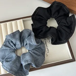 Chouchous en denim noir et bleu avec coutures contrastées présentés sur bois