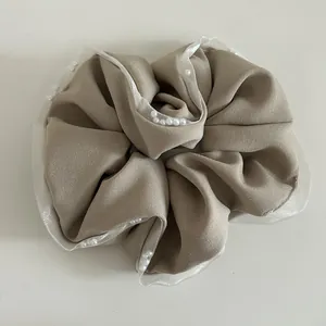 Detail of khaki scrunchie featuring white mesh lace edges and delicate pearl embellishments