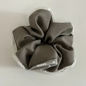 Close-up detail of mesh lace edges and white pearl beads on a brown fabric hair scrunchie