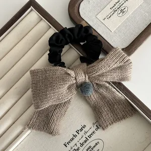 Détail d'un nœud tricoté kaki avec pompon gris sur chouchou noir élégant