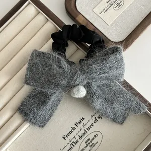 Détail d'un chouchou noeud en peluche grise avec pompon en fourrure et satin doux