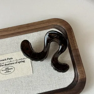 Detailansicht einer dunkelbraunen wellenförmigen Haarklammer auf einem Holztablett