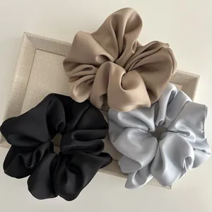 Three elegant satin oversized hair scrunchies in khaki, black, and light blue on a tray