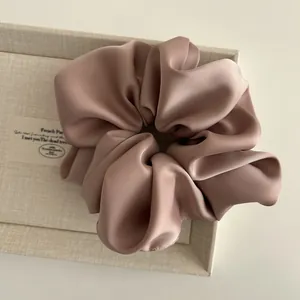 Close-up of a large dusty rose satin scrunchie with elegant pleated fabric texture