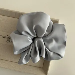Close-up of a silver-gray satin hair scrunchie with rich folds on a beige display tray