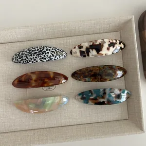 Set of 6 oval acetate hair clips with tortoiseshell and marble patterns in a beige tray