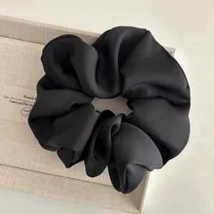Close-up of black satin oversized scrunchie with elegant pleated silk texture on beige box