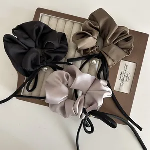 Elegante Satin-Haargummis mit langen Schleifen und Perlenanhängern auf Samttablett