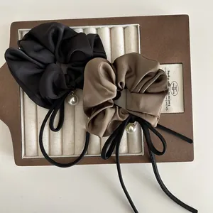 Detail von Satin-Haargummis in Schwarz und Hellbraun mit Schleife und Perlenanhänger