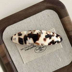 Detail view of oval tortoiseshell acetate hair clip on a natural linen background