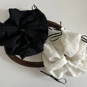 Black and off-white scrunchies with ribbons in a wooden tray on a white background
