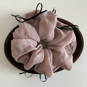 Pink oversized scrunchie with pleated fabric texture and delicate black ribbon bows
