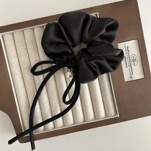 Detail eines schwarzen Satin-Haargummis mit Schleife, Seidenfinish und weißer Perle