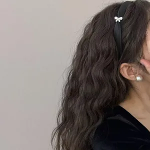 Détail d'un serre-tête en satin noir avec nœud blanc sur cheveux ondulés
