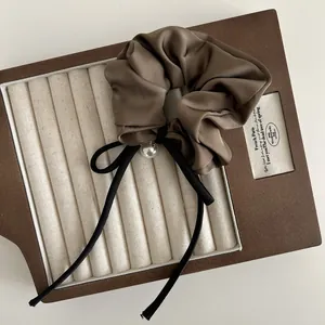 Nahaufnahme von Satin-Haargummi mit weißem Perlenanhänger auf braunem Display-Tablett