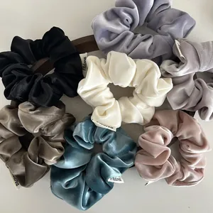 Elegant velvet hair scrunchies in various solid colors displayed on a wooden base