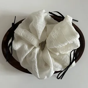 Detail of a large cream-colored scrunchie with delicate black satin bows on a wood tray