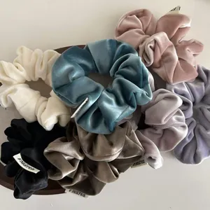 Detailed view of assorted velvet scrunchies with brand labels in a wooden tray
