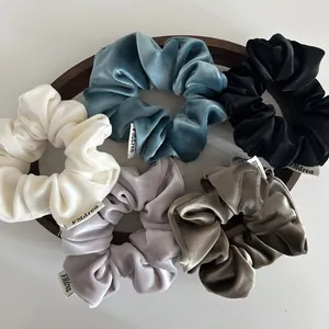 Set of five premium velvet scrunchies in elegant solid colors on a wooden tray