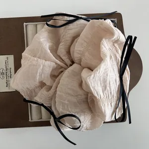 Detail of beige pleated oversized scrunchie featuring elegant black ribbon bows
