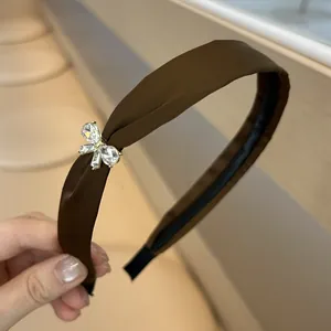 Gros plan d'un serre-tête en satin marron foncé orné d'un nœud en strass brillant