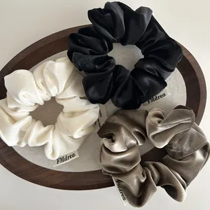 Three premium velvet scrunchies in cream, black, and mocha brown colors on a tray