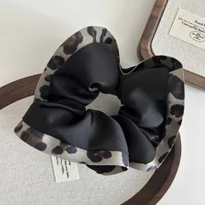 Close-up of leopard print and black satin scrunchie with elegant ruffled texture