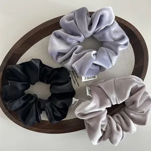 Detailed view of three velvet scrunchies in black, purple, and grey on a display tray