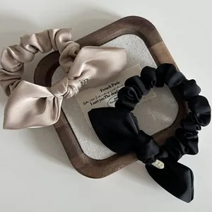 Satin bow scrunchies with heart pendants in black and champagne gold on a wood tray