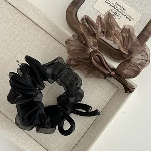 Detail of sheer organza bow hair scrunchies in black and brown on a vintage tray