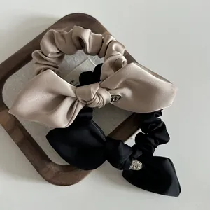 Detailed macro of satin bow scrunchies with metal labels in champagne and black