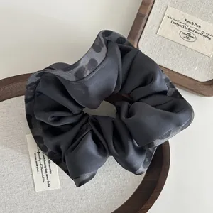 Close-up of leopard print satin scrunchie detail in a wooden jewelry display tray