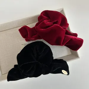 Detail view of burgundy and black velvet hair clips with a gold logo and soft folds