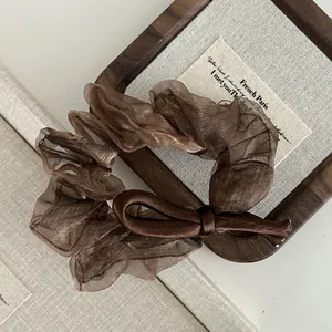 Close-up of a brown satin bow scrunchie featuring elegant pleated organza textures
