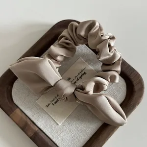 Close-up of champagne satin scrunchie with elegant bow and metallic detail on a tray