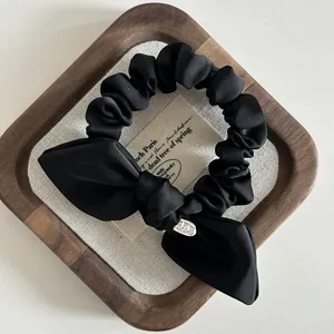 Detail of black satin bow scrunchie featuring an oval metal tag on a wooden tray