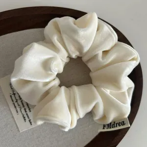 Close-up of a plush cream velvet scrunchie featuring a brand label in a wooden tray