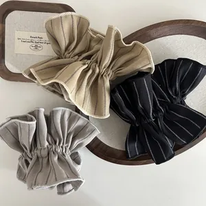 Three striped oversized scrunchies in khaki, black, and grey on a wooden tray