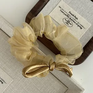 Detailed close-up of champagne gold organza scrunchie with silk bow on a wooden jewelry tray