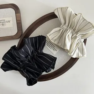 Detail showing striped pleated fabric scrunchies in black and beige on a wooden tray