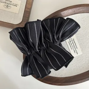 Close-up of black striped scrunchie with layered pleated design on a wooden tray