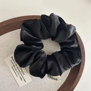 Elegant black velvet scrunchie hair tie with rich folds and premium brand woven label