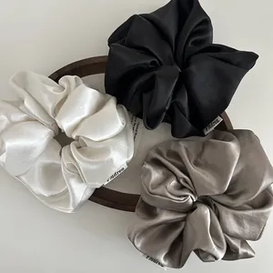 Close-up of three satin scrunchies in cream, black and champagne with woven labels
