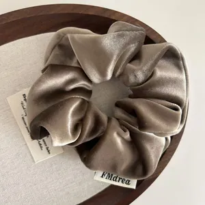 Brown velvet scrunchie hair tie with brand tag on a rustic wooden tray holder