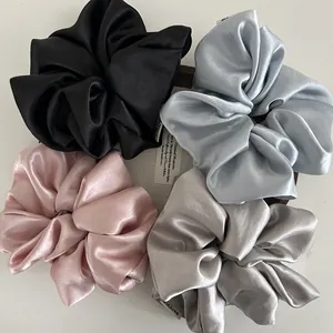 Set of four glossy satin hair scrunchies in black, blue, pink, and grey on wood tray