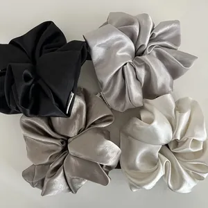Close-up of four large satin scrunchies in black, silver, champagne, and cream silk colors