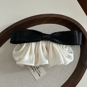 Détail d'une pince à cheveux nœud en satin avec bord plissé ivoire sur plateau en bois