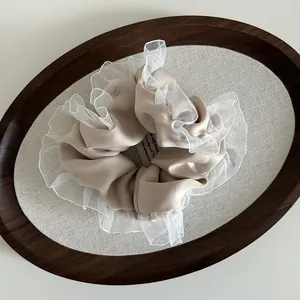 Detailed close-up of a beige fabric hair scrunchie with layered white lace ruffles on a tray