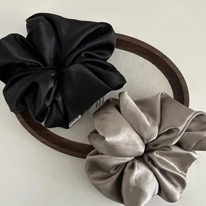 Set of large black and champagne satin scrunchies displayed on a wooden tray
