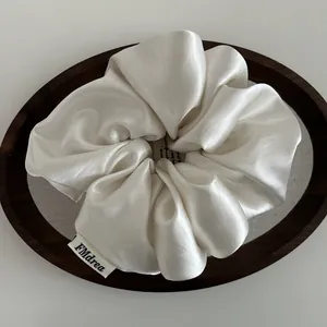 Close-up of white satin scrunchie with FMdrea brand label on a wooden tray